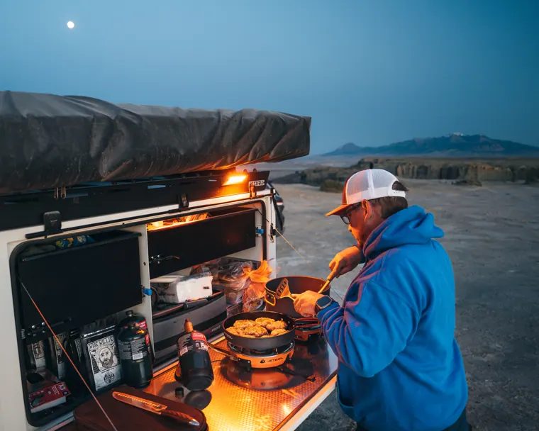 Off-road camper trailer set up at camp at dusk with lights on