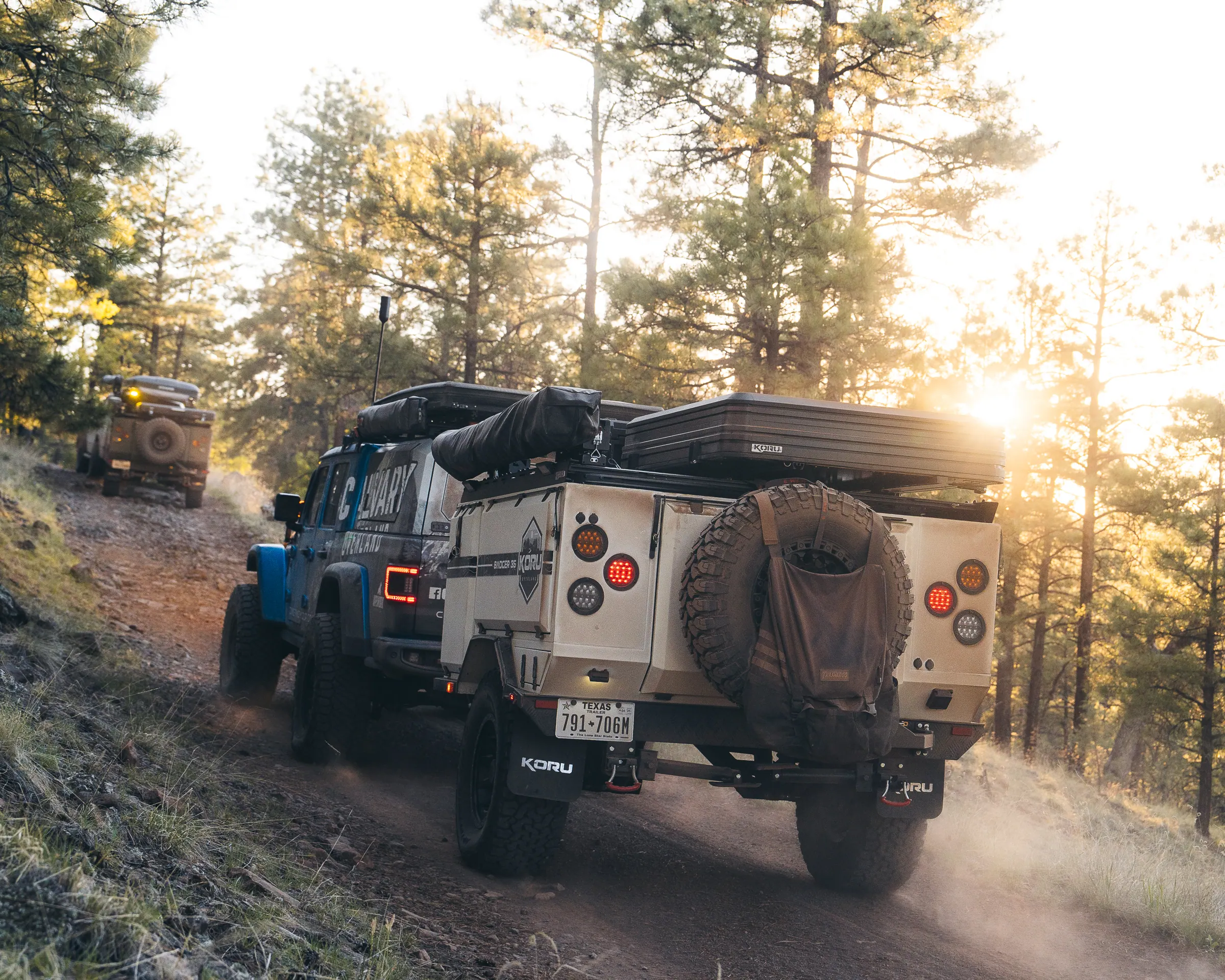 A Koru Badger trailer kicking up dust on a forest trail at golden hour